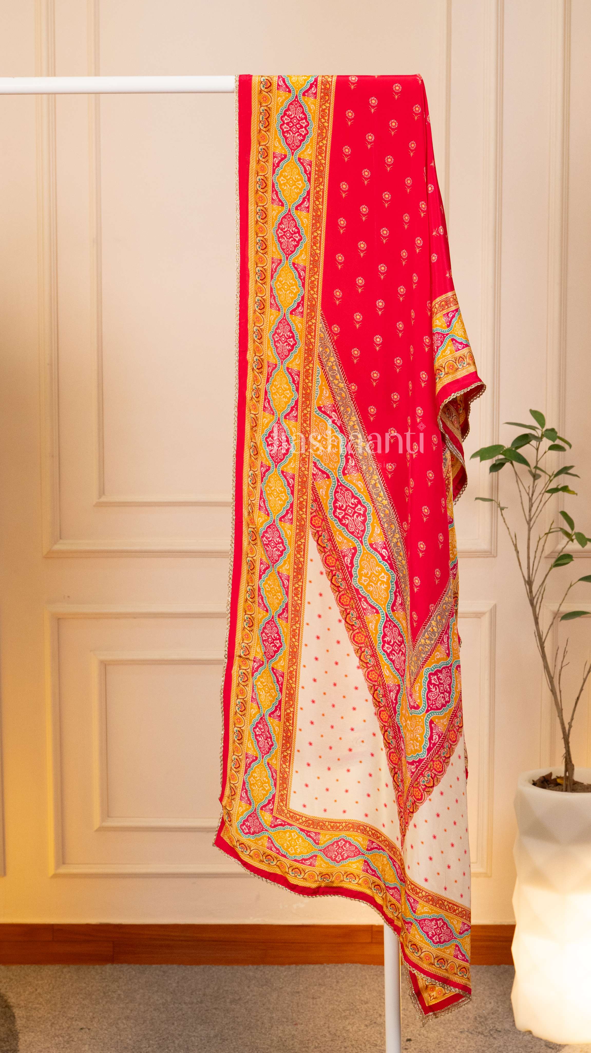 Red and yellow patterned fabric draped over a white rod against a beige wall.
